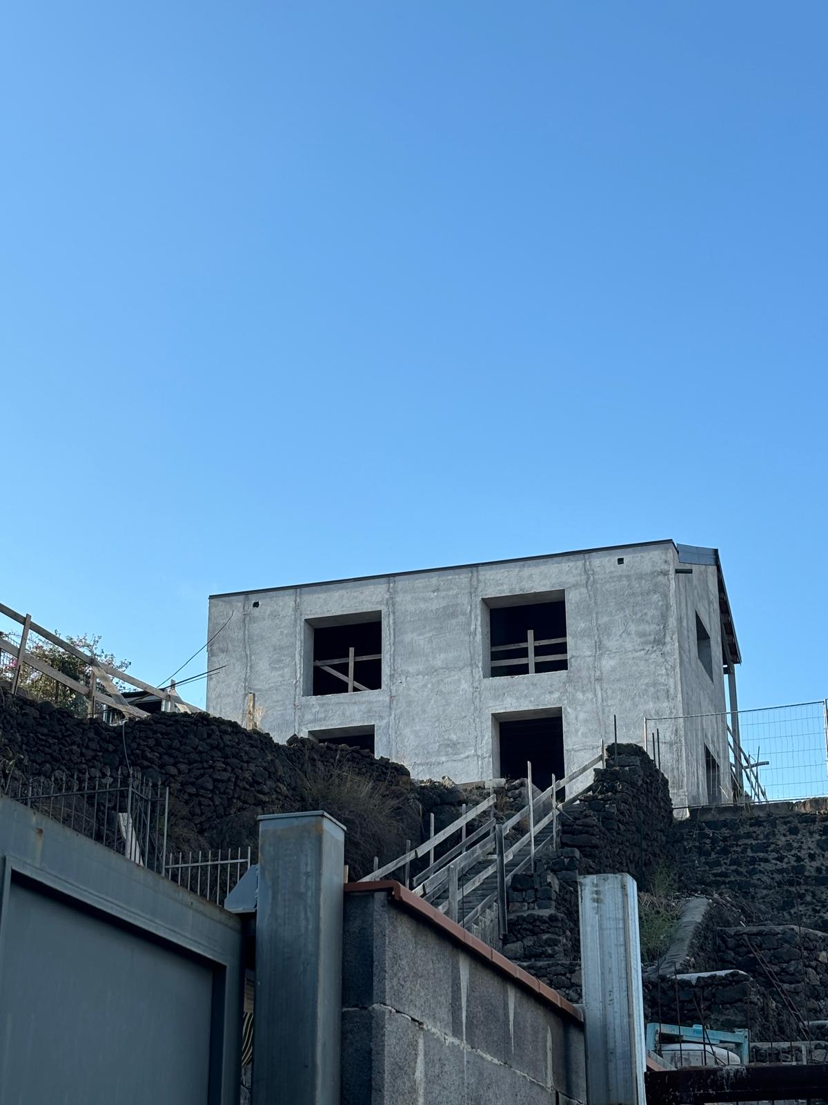 Casa incompiuta su un pendio, tra muri di pietra e cielo azzurro